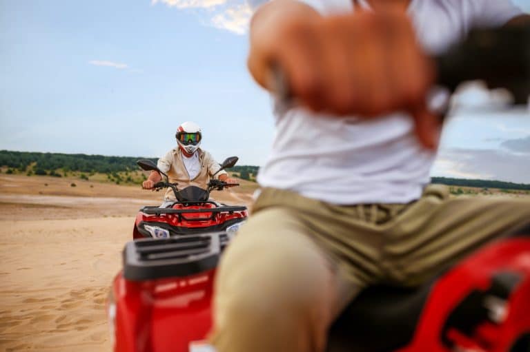 deux personnes qui font du quad dans le désert avec un casque